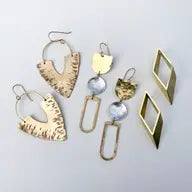 Assorted handmade statement earrings in brass, silver, and geometric designs on a light background.